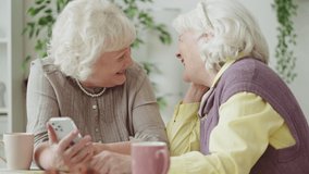 Two happy senior women watching funny video on phone and laughing, social media