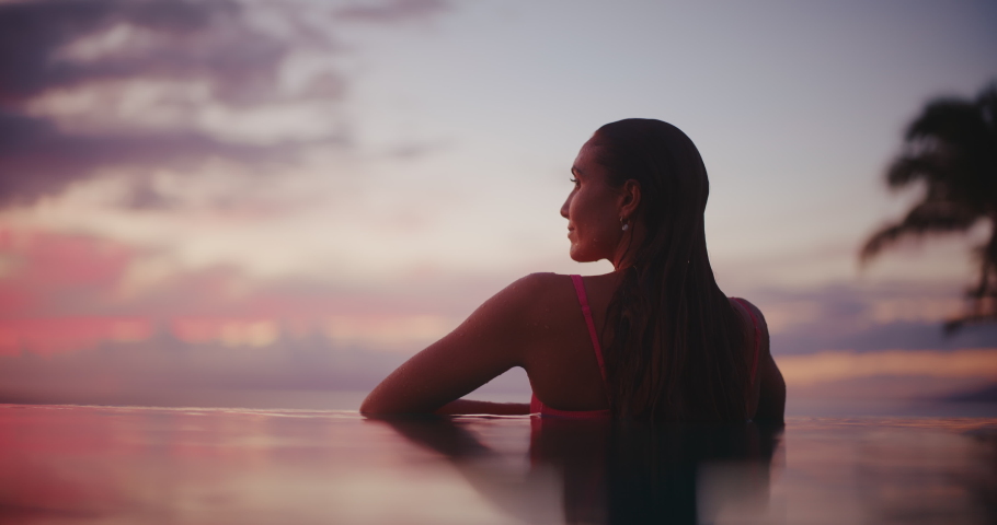 Woman relaxing in luxury infinity pool, looking out over the ocean at sunset, tropical resort spa vacation