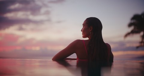 Woman relaxing in luxury infinity pool, looking out over the ocean at sunset, tropical resort spa vacation Arkistovideo
