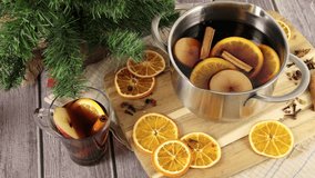 Woman's hand grabbing a glass mug with mulled wine drink from wooden table with Christmas decorations, hot scented wine with cinnamon, star anise, orange fruit and spice, slow motion 4k video footage