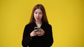 4k video of cute girl using phone and waving hello over yellow background.