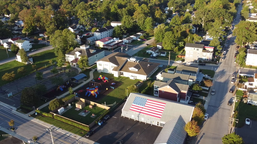 Drone aerial rotation over town in maryland with flag on rooftop as centerpiece, trees in background