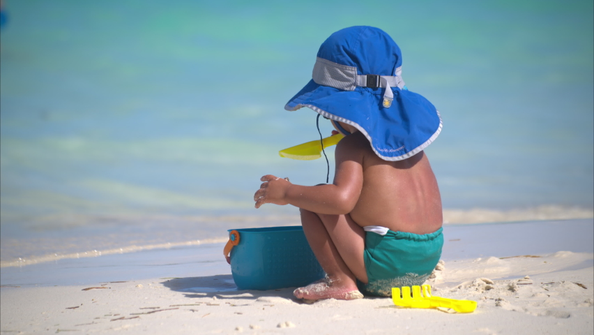 Young little baby boy playing alone on the sand at the beach with toys wearing a blue hat and a turquoise diaper in Cancun Royalty-Free Stock Footage #1097960309