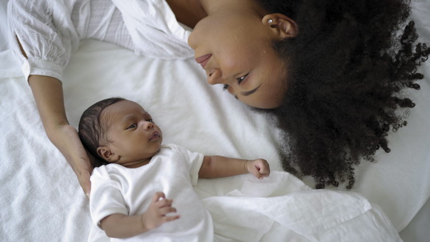 Closeup portrait of beautiful young African American mother day girl kiss healthy newborn baby sleep in bed flat lay copy space. Healthcare medical love black woman lifestyle mother's day, top view Royalty-Free Stock Footage #1097963343