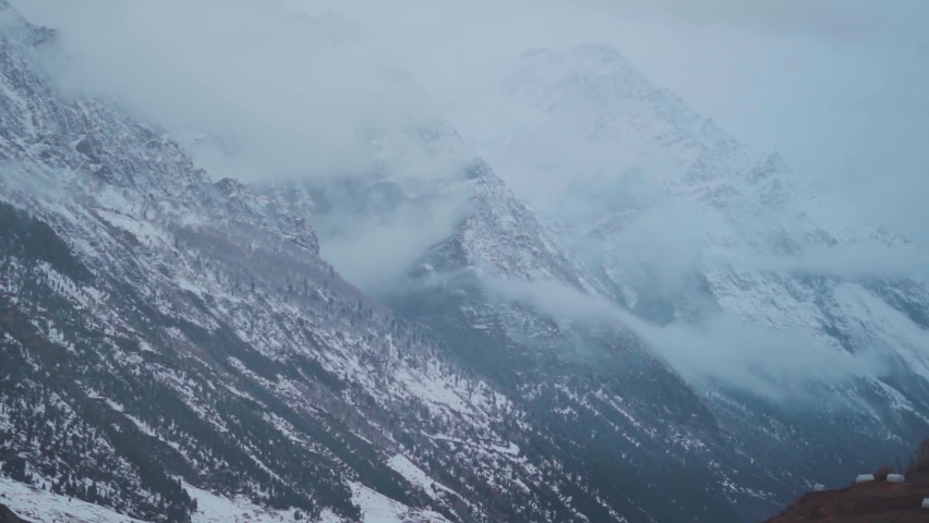Landscape shot of clouds under the snow covered Himalayan mountain peaks of Lahaul during the winter season at Lahaul Spiti in Himachal Pradesh, India. Snow storm in the mountains during the winter.