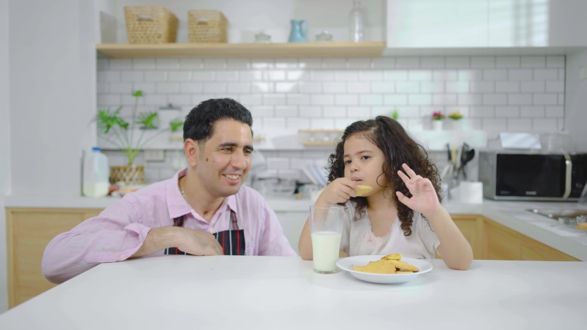 Family living together with love. Father and little daughter spending time together and having breakfast cookies and drinking milk at table in kitchen at home, Milk is beneficial