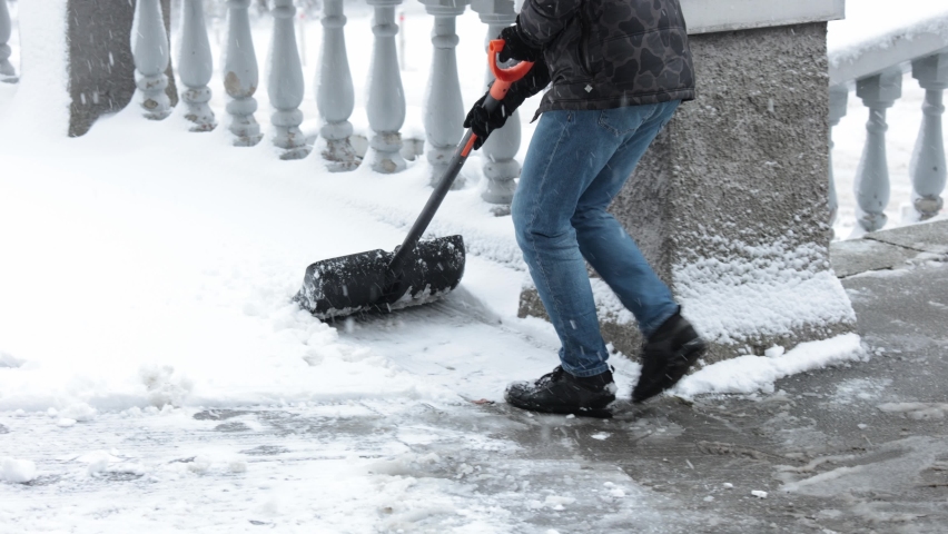Man with a shovel removes snow. Cleaning the area near the house after a snowstorm. Person shoveling snow out of the driveway. Huge snow drifts Royalty-Free Stock Footage #1097971847
