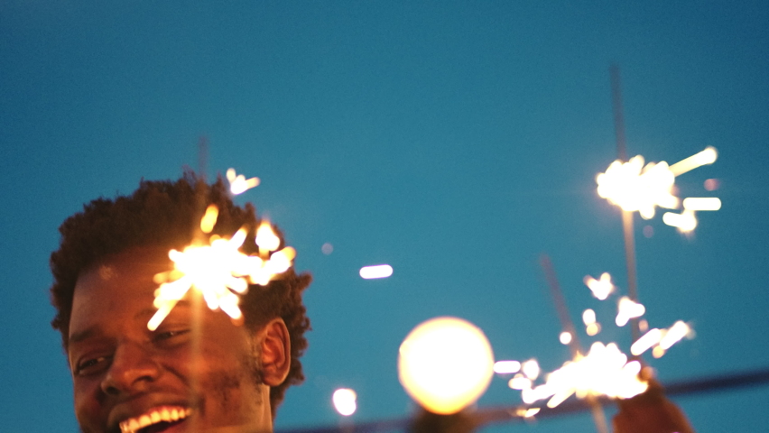 Black man, laughing or dancing and sparkler in night rooftop party, New Year celebration or birthday social gathering on building. Smile, happy or dance people with fireworks in freedom energy motion Royalty-Free Stock Footage #1097972311