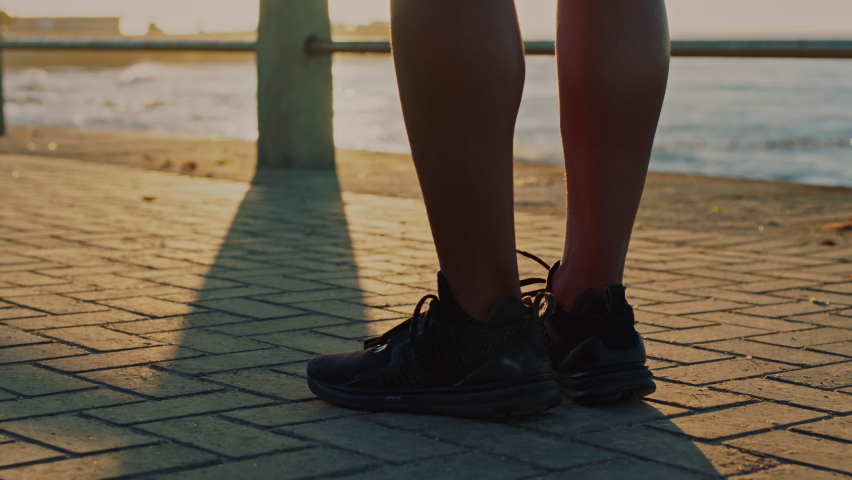 Fitness, shoes and man stretching feet for running on beach promenade, marathon and silhouette in sunshine outdoor. Closeup shadow of runner, sneakers and ready to start exercise on beach sidewalk