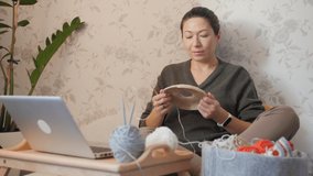 Close-up video of woman learning to crochet. Felt basket with balls of yarn. Anti-stress hobby. Online lessons for amateurs on laptop.