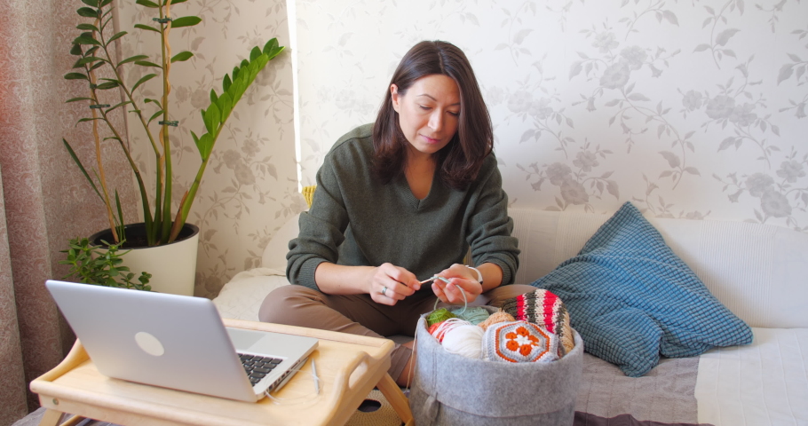 Close-up video of woman learning to crochet. Felt basket with balls of yarn. Anti-stress hobby. Online lessons for amateurs on laptop.