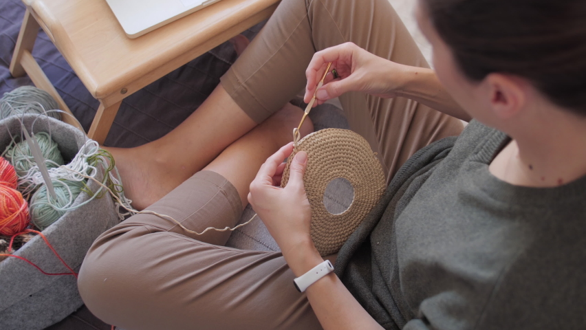 Close-up video of woman crocheting bag of polyester cord. Anti-stress hobby. Tranquil leisure at home. Handicraft. Online lessons for amateurs on laptop.