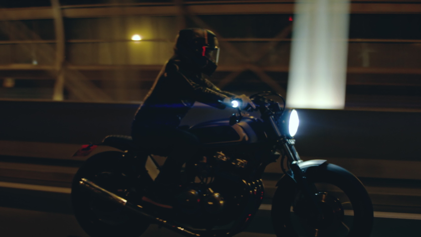 TRACKING Shot of a biker riding his custom built cafe racer motorcycle through city at night. Shot with 2x anamorphic lens Royalty-Free Stock Footage #1097981319