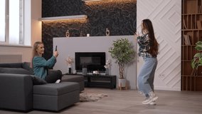Side view of two girls recording video on smartphone camera. Pretty young woman shooting her friend dancing hip hop in the living room or in the studio. High quality footage