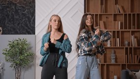 Two young attractive students dancing hip hop in front of the camera in modern living room. Happy friends recording a video for social media. High quality footage