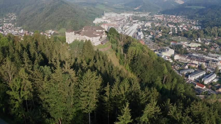 aerial photography, wide drone establishing shot of Burg Oberkapfenberg in Kapfenberg Austria, in soft morning light, with Böhler steel works and the city in the background, circling around the castle