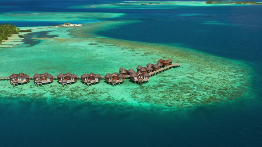 Luxury overwater villas with coconut palm trees, blue lagoon, white sandy beach at Bora Bora island, Tahiti, French Polynesia. Aerial drone view.