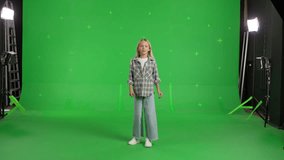 Caucasian kid dancing on a green screen background. Girl makes a gesture with her hands as if swipping the page to the side . Chroma key
