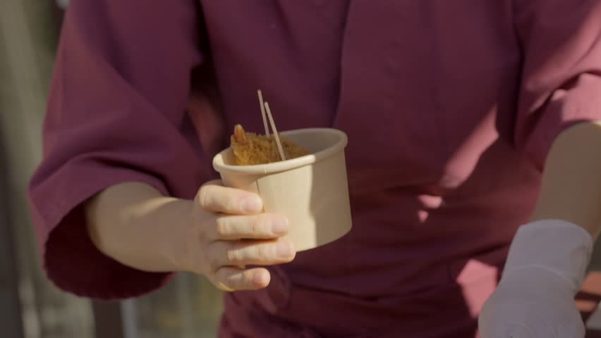 This video shows a close up view of an outdoor food vendor placing fried food items on a counter.