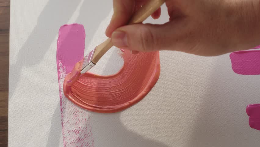 Top down young woman hand paints Peach Fuzz color with wide brush on small white canvas in daylight from sun. artist makes beautiful brush strokes on painting.Writing masterpiece picture in art studio Royalty-Free Stock Footage #1097993721