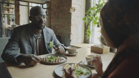 Over the shoulder shot of African American businessman eating lunch and speaking with female colleague in hijab at cafe table - Powered by Shutterstock - Get 15% off with code: PIKWIZARD15