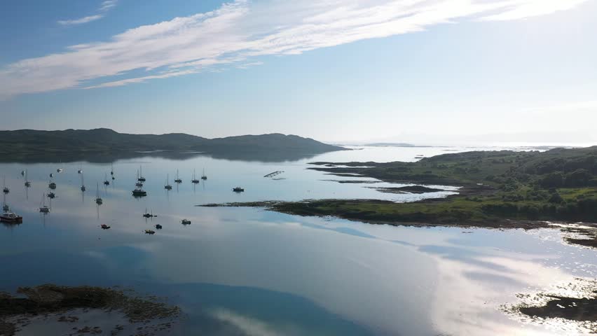 Aerial footage flying out of Arisaig Harbour towards Isle of Eigg. Sunny day with sky reflection on sea