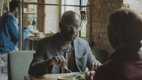 Over the shoulder shot of African American man eating lunch and talking with woman in hijab at table in cafe - Powered by Shutterstock - Get 15% off with code: PIKWIZARD15