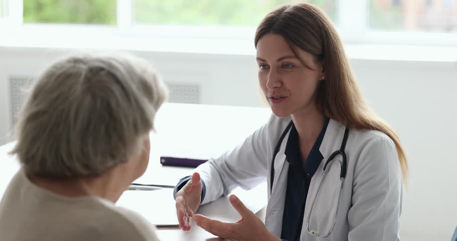 Close up of professional woman physician or cardiologist in white coat consults older female patient sit at table in clinic share prescriptions, gives advices about health, provide support. Eldercare Royalty-Free Stock Footage #1098002573
