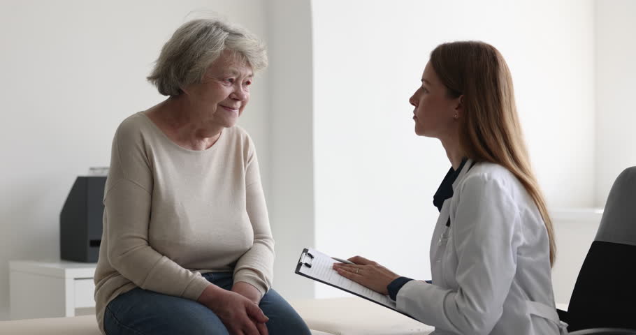 Female doctor in white coat listen to older woman tell about chronic disease, health complaints, affliction symptoms, therapist take notes, fill history form during patient visit. Nursing, elder care | Shutterstock HD Video #1098002585