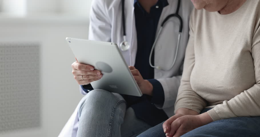 Cropped close up view unknown elderly patient listen to woman doctor during visit in clinic, gp teach older female to use new medical application, show health test results on tablet device. Healthcare Royalty-Free Stock Footage #1098002623