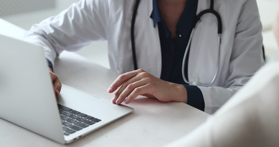 Unknown female cardiologist or general practitioner, professional medical worker in white coat talks to client seated at table with laptop, close up. Medicine, treatment, prescriptions, health-care | Shutterstock HD Video #1098002669