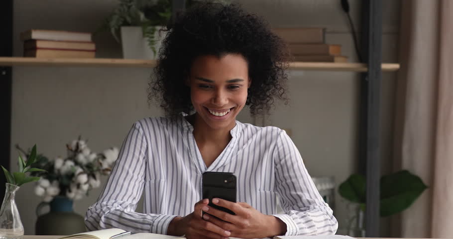 Distracted from studying happy millennial African American woman in playing mobile games, web surfing information, watching funny photo video content in social network, communicating or shopping. | Shutterstock HD Video #1098004941