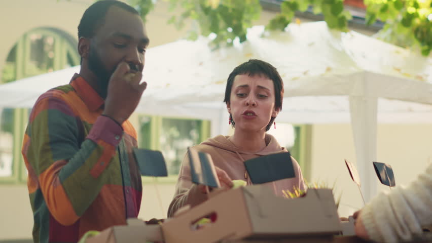 Female farmer giving free slices of apples for clients to taste, diverse people enjoying product samplingg at food market. Young woman giving samples of organic produce to cusomers. Handheld shot.