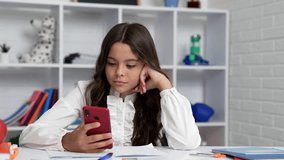serious child chatting using smartphone in classroom, school