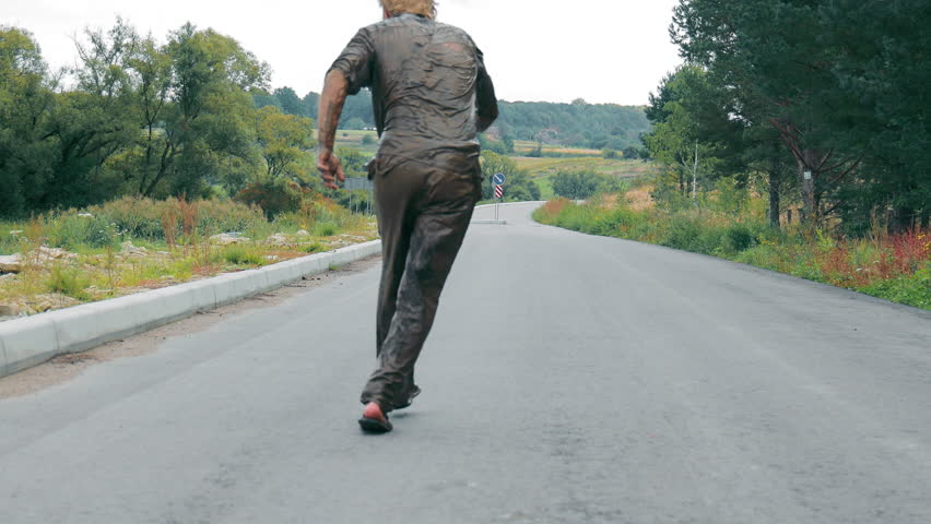 Rear view A drunk and dirty man walks along the road. An alcoholic and a homeless man covered in swamp strud walks down the street.