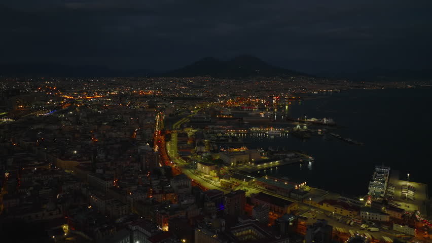 Aerial view of city harbour and surrounding urban boroughs at night. Majestic Mount Vesuvius silhouette in distance. Naples, Italy Royalty-Free Stock Footage #1098009367