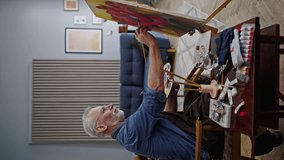 Vertical video of inspired elderly Caucasian man with gray hair and beard, a talented experienced artist painter at retirement, enjoying painting on canvas in creative art workshop on his free time
