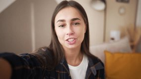 Smiling young caucasian woman vlogger make video call, looking at camera, recording vlog at home, talking. View from front camera to portrait video recording, girl holds mobile phone in hands.