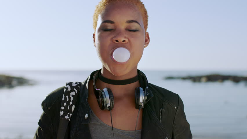 Young black woman, face and bubble gum outdoor at beach, travel and holiday in Atlanta. Chewing gum bubbles, sweets and candy at ocean with playful, funny and happy gen z girl, happiness and freedom Royalty-Free Stock Footage #1098019415