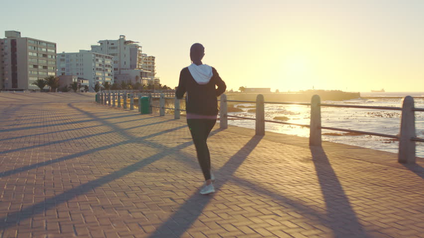 Woman runner, islam and beach with hijab in summer sunset for health, fitness and wellness in city. Muslim female athlete, running and training by ocean for workout, freedom and exercise in Beirut Royalty-Free Stock Footage #1098020033