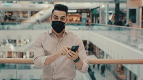 Confused businessman guy man in medical face mask has problem with app smartphone notification. Male entrepreneur in shopping mall looking at camera displeased puzzled pointing to mobile phone screen - Powered by Shutterstock - Get 15% off with code: PIKWIZARD15