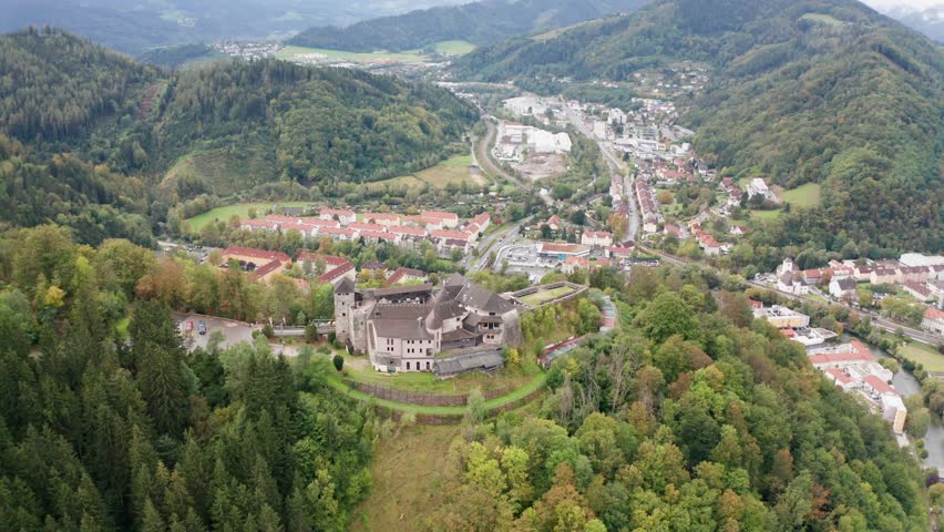 aerial photography, wide drone establishing shot of Burg Oberkapfenberg castle in Kapfenberg Austria, with Böhler steel works and the city in the background, circling around the castle from a distance