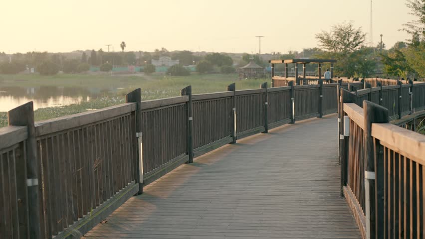 A long wooden pedestrian bridge over a lake at sunset.