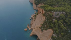 Top view of a rocky shore covered with green trees. Cave in the rock. Blue clear water. Seascape. Drone video footage