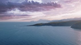 Aerial drone video footage. Seascapes at sunset. Blue sea and green trees on the shore. Mountains in the background 