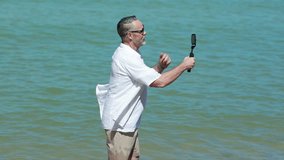 Senior caucasian male holding smart phone in hand shooting selfie photo on the beach. Vacation trip summer holiday.