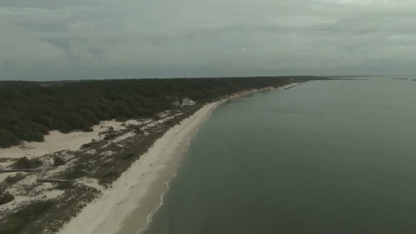 High aerial panning above east coast beach, trees and white beach house on cloudy day