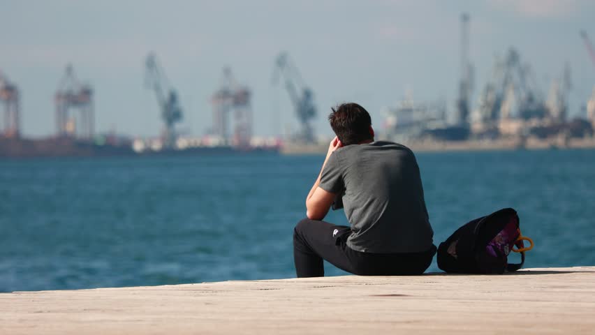 Young man sitting at seaside near harbor, Thessaloniki Greece