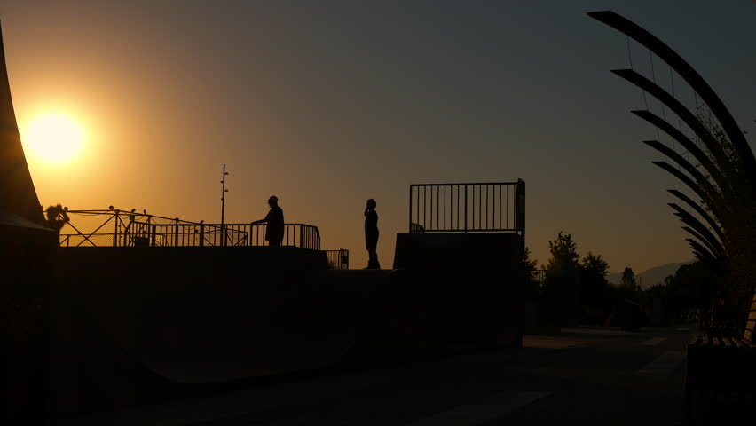 Sporty teens on rollers at sunset. A view of sporty teen on rollers play on the playground in sunset. A concept of happiness and sporty lifestyle during teen's life.