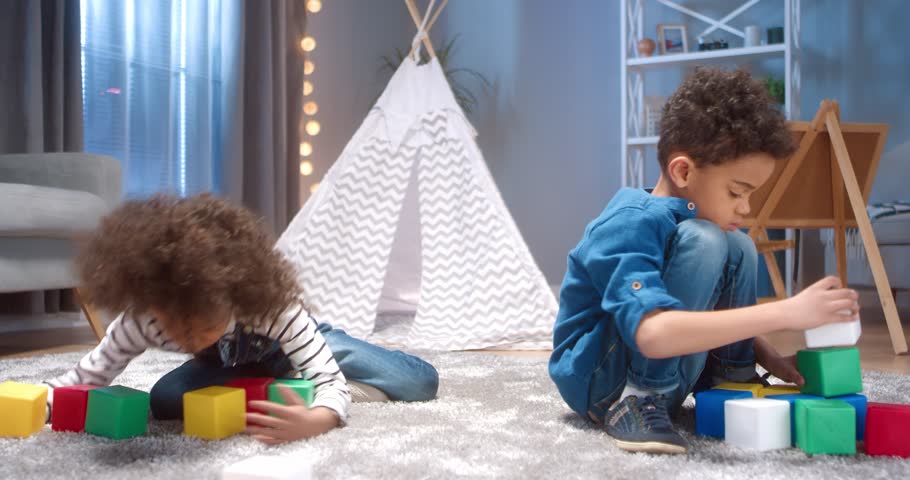 Little African-American girl with the curls resentful and greedily covers the toys while her brother is docile playing alone. Royalty-Free Stock Footage #1098055247